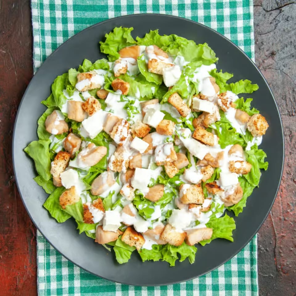 Niki's Caesar salad with fresh lettuce, croutons, chicken, and creamy dressing on a dark plate.