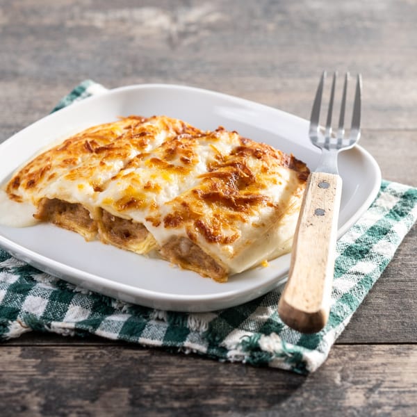 Niki's cannelloni with melted cheese on a white plate with a fork and checkered napkin.