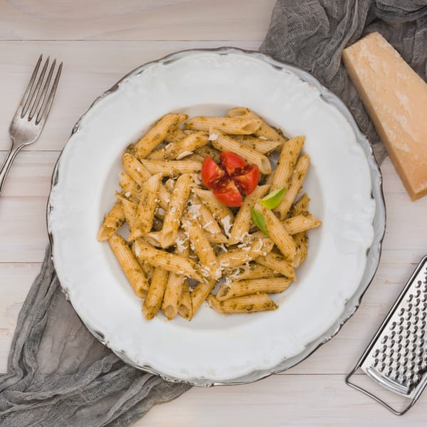 Niki's penne pasta with pesto, grated cheese, tomatoes, and basil, with a grater and parmesan.