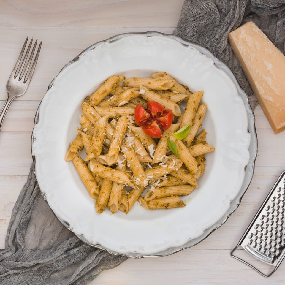 Niki's pesto penne pasta with cherry tomatoes, parmesan, and basil on a white plate.