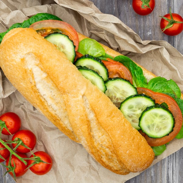 Niki's Italian sub sandwich with fresh tomatoes, cucumbers, and lettuce on a wooden table.