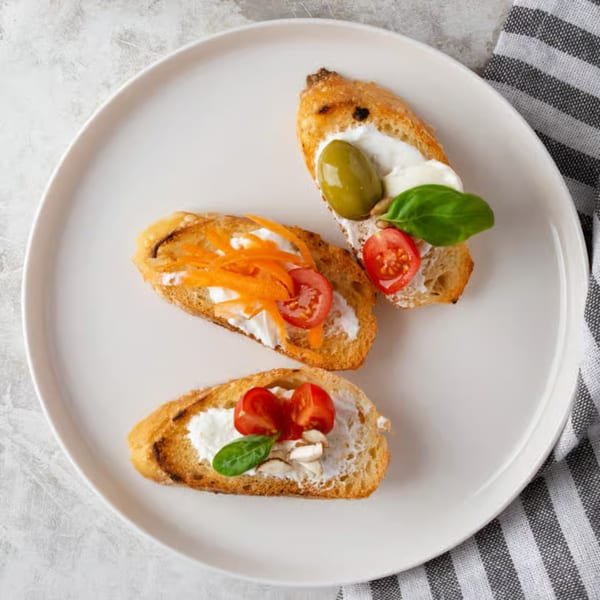 Three Italian bruschetta appetizers with various toppings on a white plate with a striped napkin.